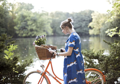 Side view of mid adult woman with bicycle standing by lake in park