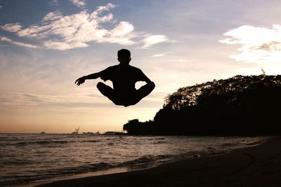 Silhouette man jumping at beach against sky during sunset