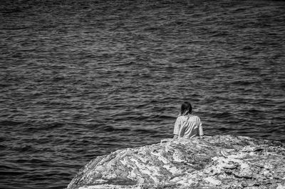 Rear view of man sitting on rock by sea