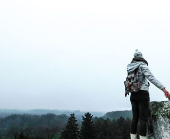 Woman standing in forest against sky during foggy weather