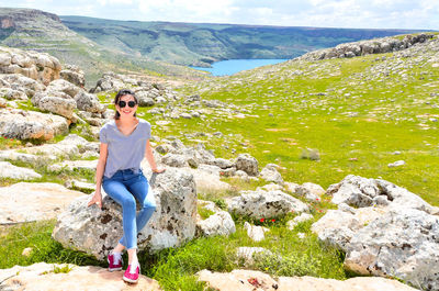 Young woman sitting on rock against landscape