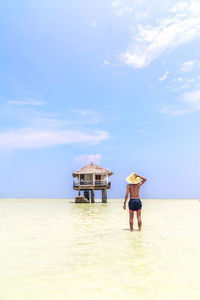 Rear view of woman standing at beach against sky