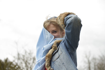 Portrait of woman holding fabric against sky