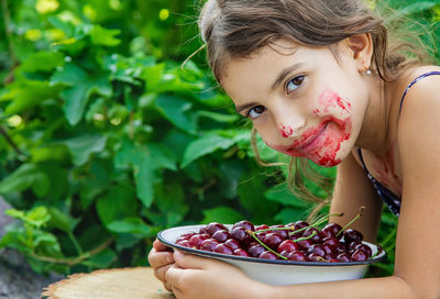 Portrait of smiling girl with messy face holding bowl of cherries