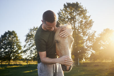 Man is embracing of therapy horse on meadow at sunset. 