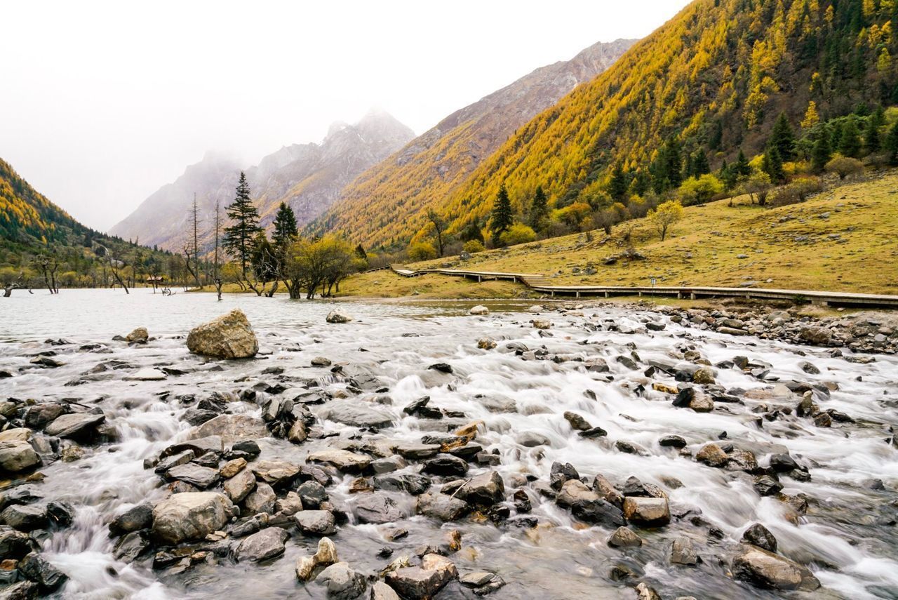 SCENIC VIEW OF STREAM FLOWING BY MOUNTAINS AGAINST SKY