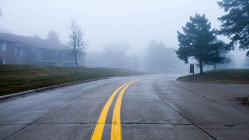 Road by trees against sky during foggy weather