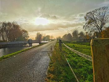 Road amidst field against sky during sunset