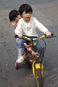 Cute boy riding tricycle with sister on road