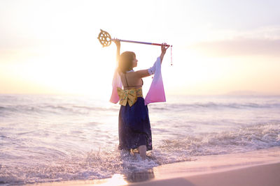 Young woman wearing costume holding wand at beach during sunset