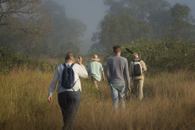 Rear view of people hiking on field against sky
