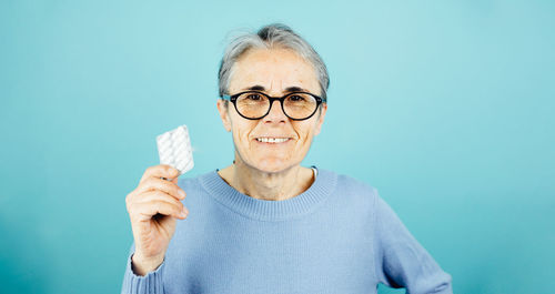 Portrait of young woman drinking milk against blue background