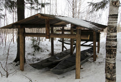 Wooden house on snow covered field by trees