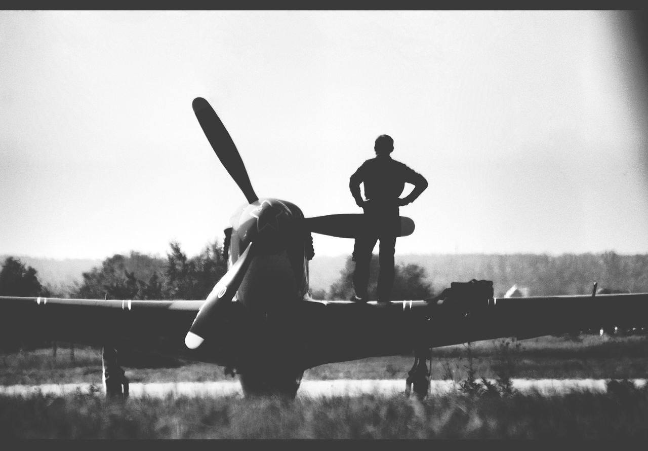 lifestyles, clear sky, men, leisure activity, silhouette, copy space, full length, water, transportation, sky, standing, outdoors, holding, hobbies, field, nature, day