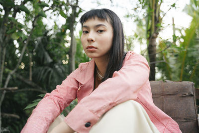 Portrait of beautiful young woman sitting against trees