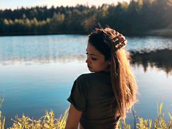 Young woman with hand in hair standing against lake