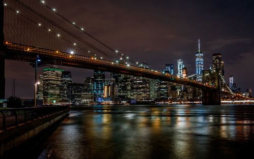 Illuminated bridge over river against sky in city at night