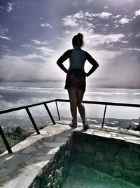 Rear view of woman standing on railing against sea