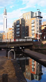 Bridge over river by buildings in city against sky