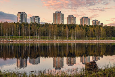 Scenic view of lake by buildings against sky during sunset