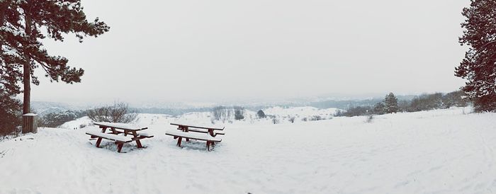 Snow covered picnic tables on field against sky