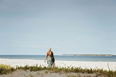 Rear view of man standing on beach against sky