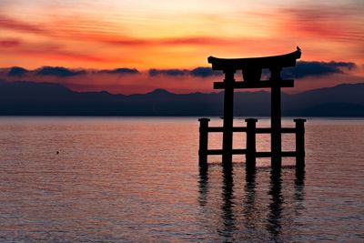 Silhouette gazebo on lake against romantic sky at sunset