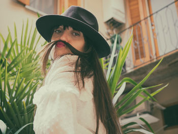 Portrait of young woman wearing hat standing against building