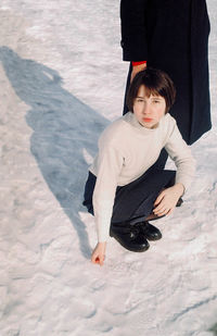 High angle view of woman crouching at snow covered field