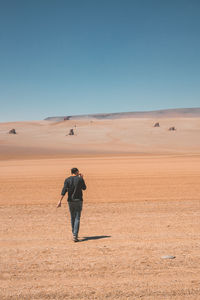 Rear view of man walking on desert against clear sky