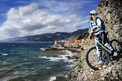 Woman riding bicycle on mountain by sea against sky