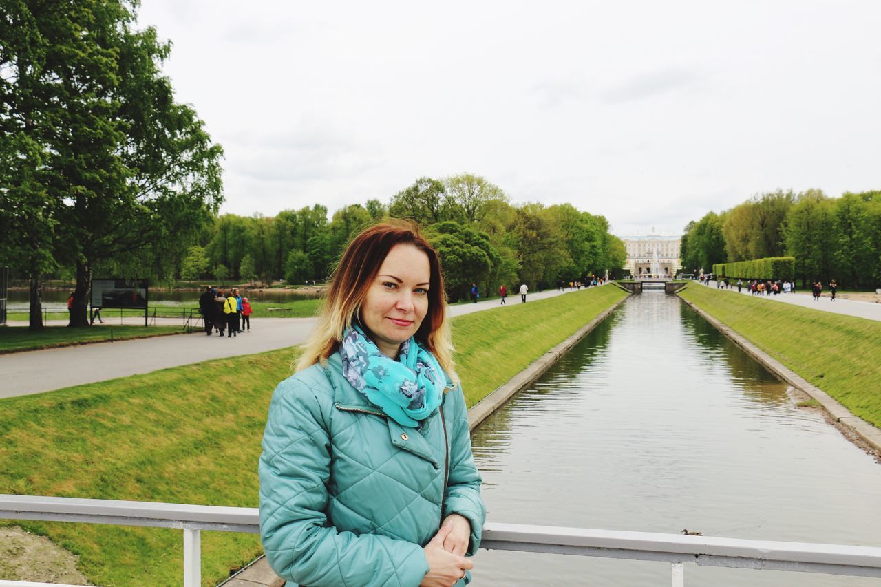 real people, one person, tree, looking at camera, young women, day, casual clothing, lifestyles, portrait, young adult, leisure activity, outdoors, smiling, park - man made space, sky, built structure, nature, standing, women, architecture, people