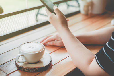 Cropped image of woman using mobile phone by coffee on table