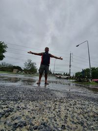 Rear view of man with arms outstretched standing against sky