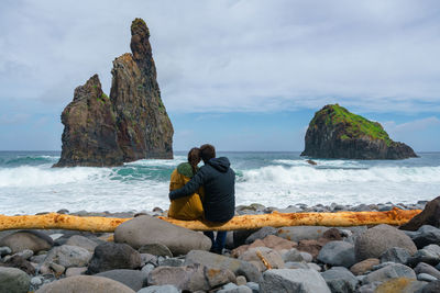 Rear view of woman sitting on rock at beach against sky