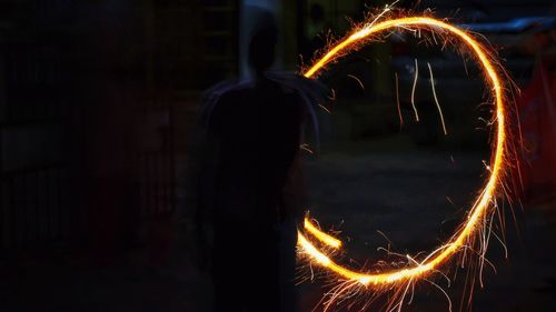 Silhouette person spinning wire wool at night