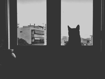 Silhouette buildings against sky seen through window