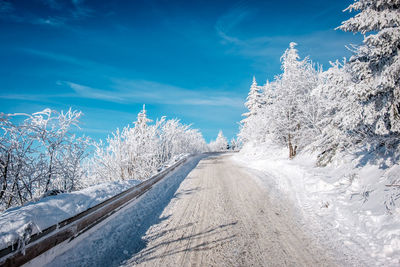 Snow covered road by trees against blue sky