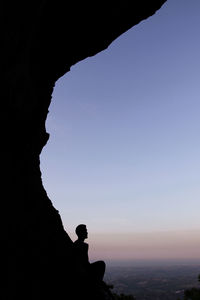 Silhouette person on rock against clear sky