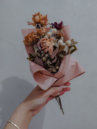 Close-up of hand holding bouquet against white background