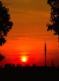 Silhouette pole and city against sky during sunset