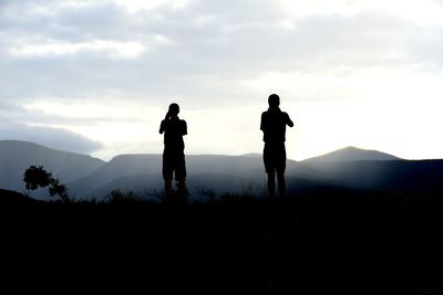 Silhouette men standing on field by mountains against sky