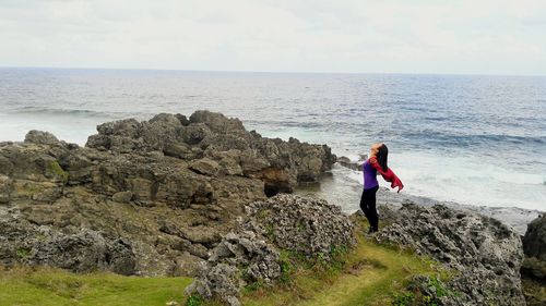 Woman standing on cliff by sea against sky