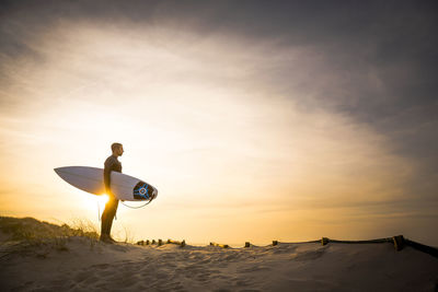 Rear view of man standing on beach against sky during sunset