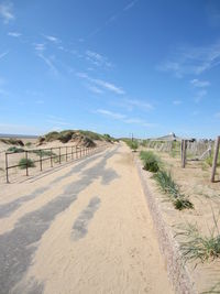 Road leading towards beach against blue sky