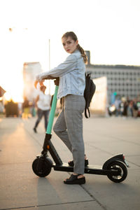 Portrait of young woman standing on push scooter against sky