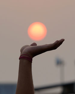 Close-up of hand holding sun against sky during sunset