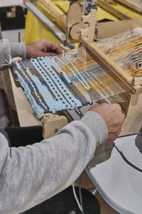 Hands of man weaving small rug with pattern on manual table loom.