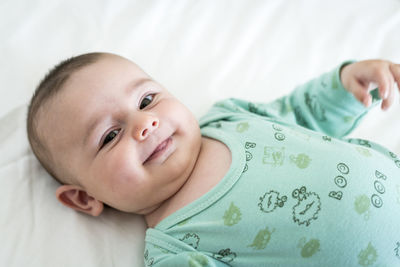 Close-up portrait of smiling toddler lying on bed at home