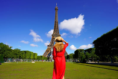 Back view of young woman looks at the eiffel tower from champ de mars in paris, france.